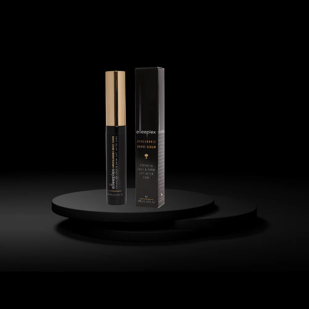 Black and gold skincare serum bottle with packaging on a black platform against a black background